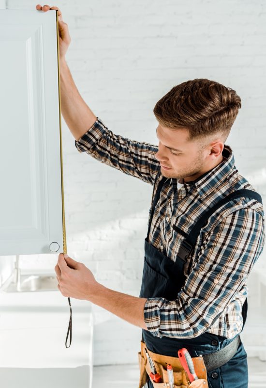 handsome installer in overalls measuring white kitchen cabinet door handsome installer in overalls measuring white kitchen cabinet door