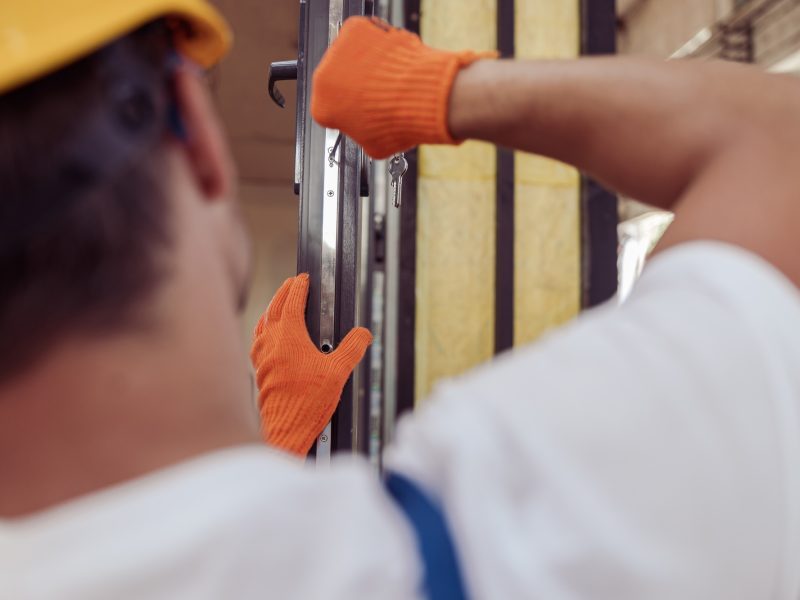 Male worker repairing door in building under construction